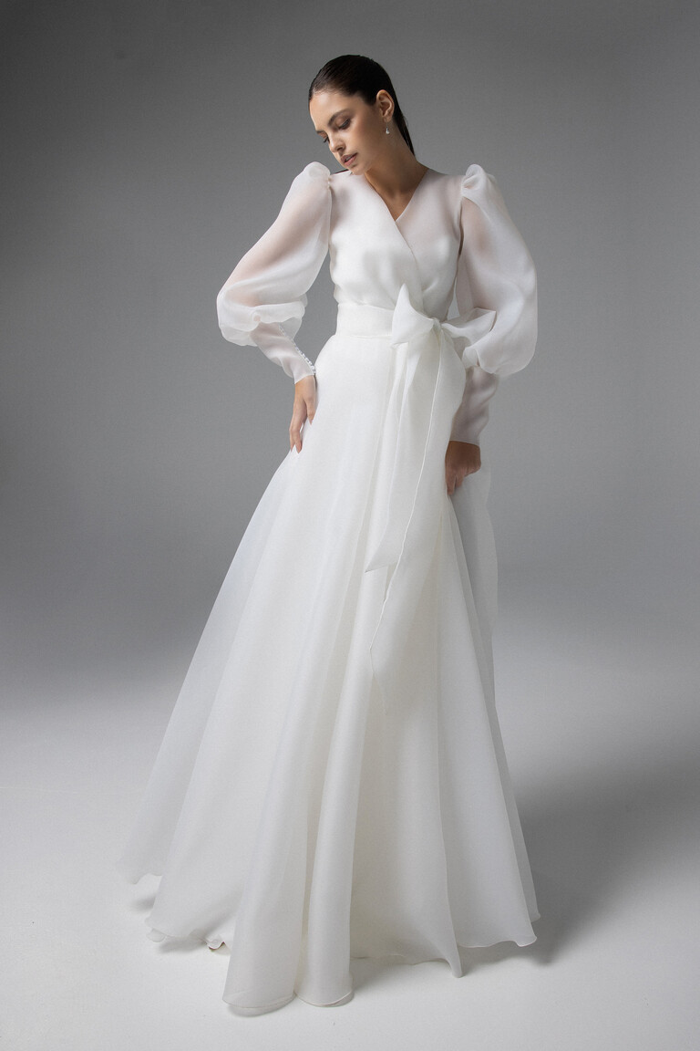 Cape Sonia Ivory Bridal Wrap with Romantic Front Bow Detail Cape Sonia ivory organza bridal wrap featuring a V-neck wrap bodice, long puff sleeves, and a front waist bow tie.