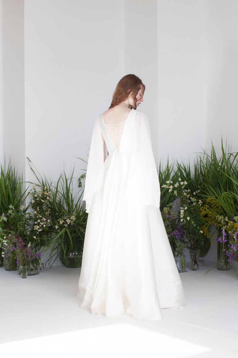 Styled back view of Edite boho ivory satin bridal gown featuring a corset lace up closure and draped chiffon cape sleeves