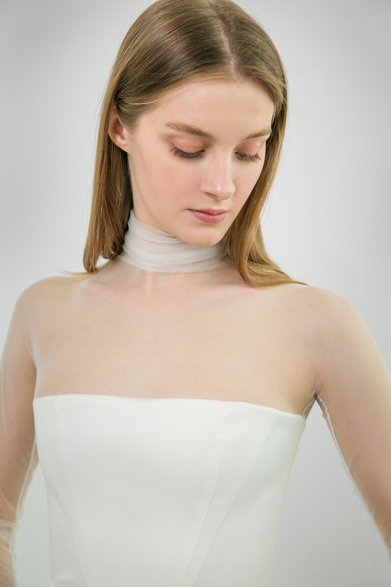Close-Up of Liz Gown Gathered High Neckline Close-up of Unona Liz ivory wedding dress. Detailed view of the gathered illusion high neckline and sheer mesh long sleeves.