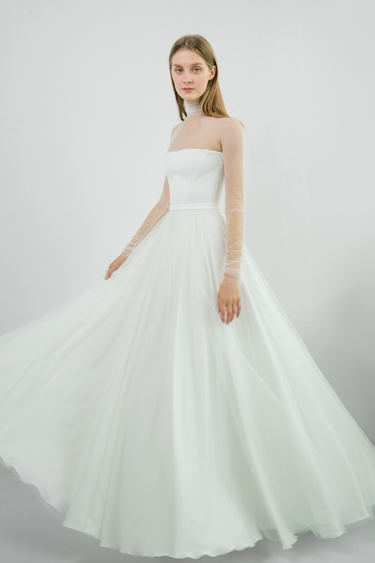 Flowing Liz Ivory A-Line Wedding Dress Full Length Unona Liz ivory A-line wedding dress front view. Illusion high neck, long sleeves, and flowing mesh skirt in motion.