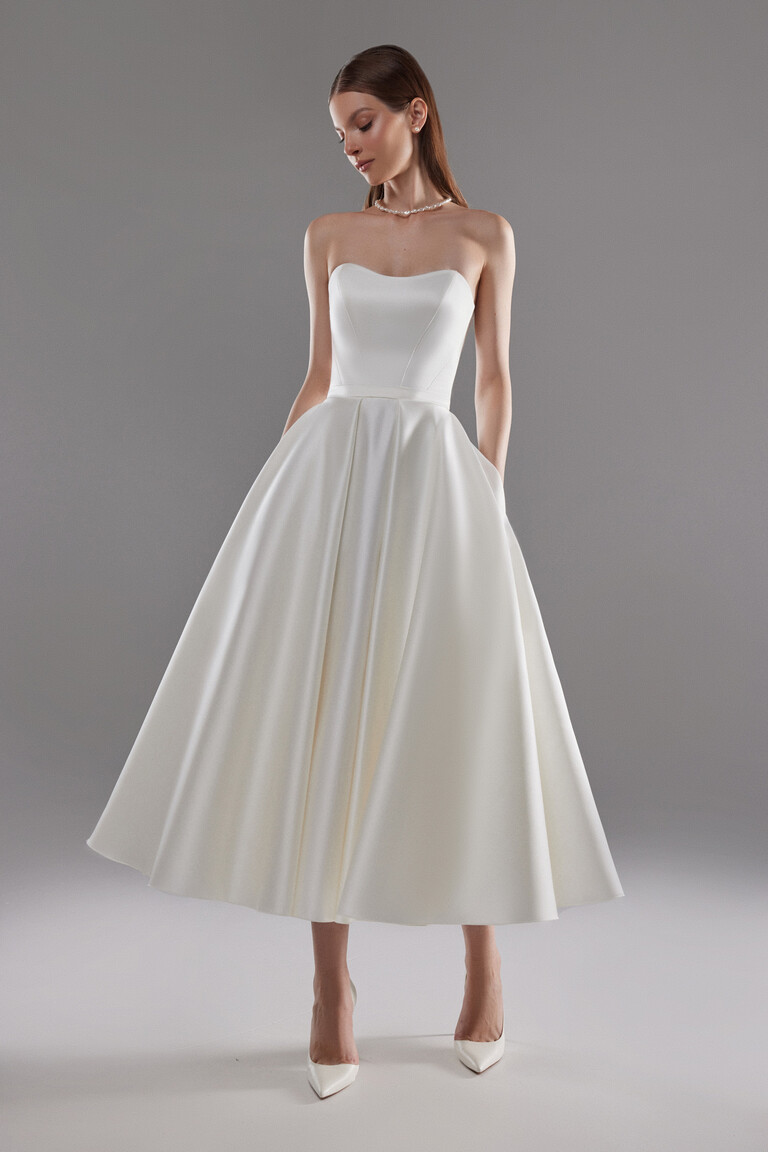 Full-length front view of Lizzie ivory satin midi wedding dress with sweetheart neckline and pockets.