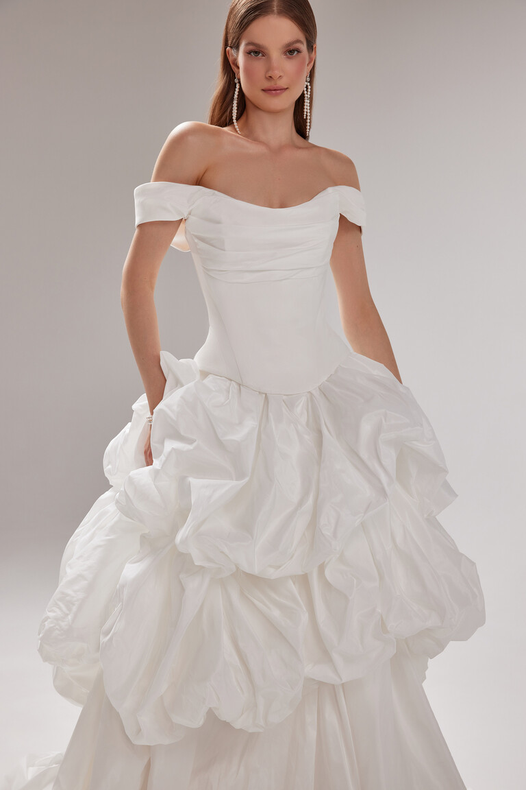 Elegant Paradise Off-Shoulder Taffeta Bridal Gown with Ruffled Skirt by Unona Unona Paradise classic off-white bridal gown. Features an off-shoulder corset bodice and dramatically draped taffeta skirt.