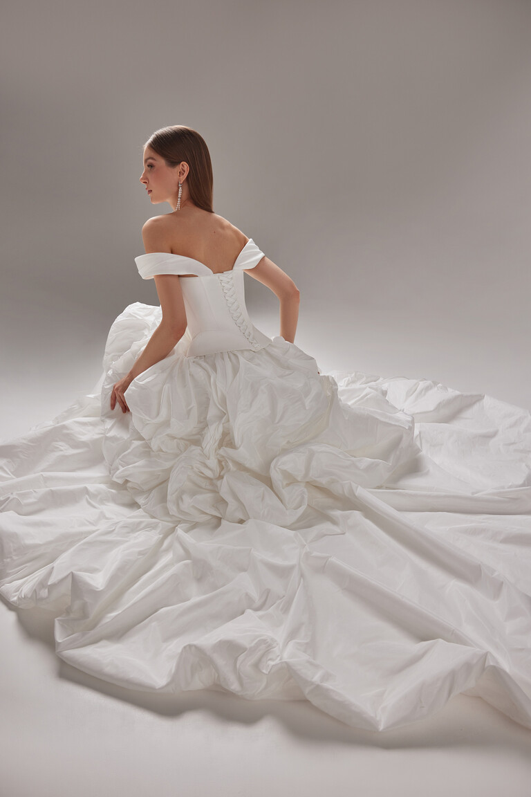 Paradise Bridal Gown Lace-Up Corset Back View and Sweeping Train by Unona Seated model in Paradise wedding dress by Unona. Highlighting the lace-up corset back and ruffled taffeta sweeping train.