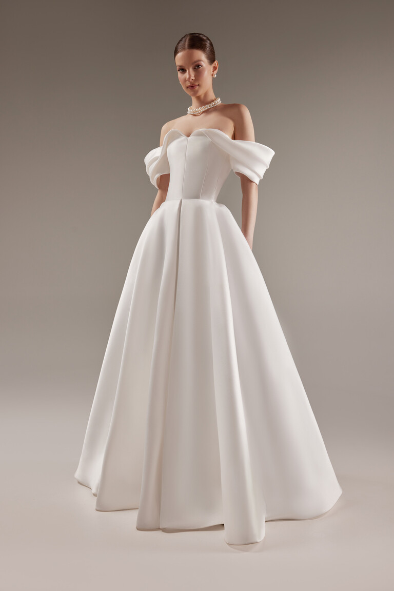 Fly Minimalist Ball Gown Front View Full-length front view of Unona Fly off-white Mikado ball gown with an off-the-shoulder sweetheart neckline.