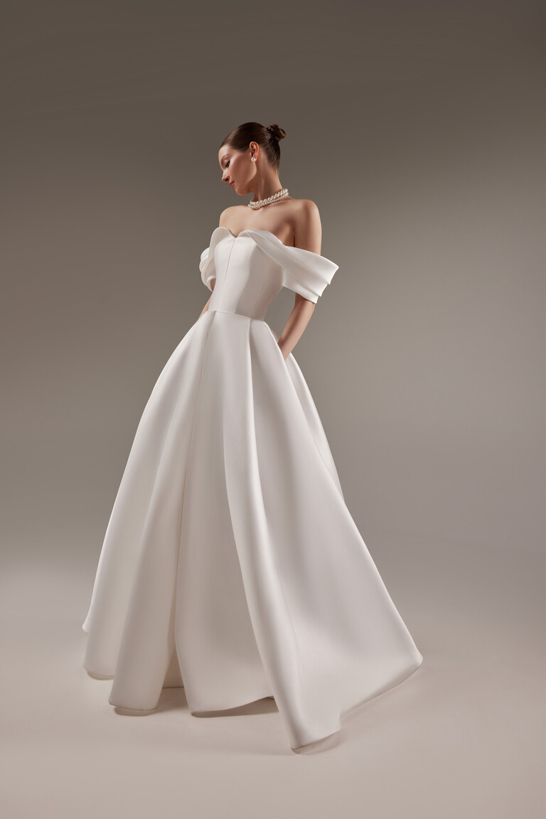 Fly Bridal Gown with Convenient Pockets Three-quarter view of the minimalist Fly off-white bridal gown highlighting its modern Mikado skirt with side pockets.