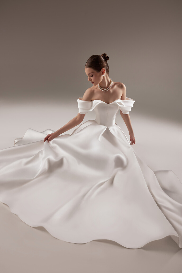 Voluminous Mikado Skirt of Fly Dress Beautiful bride sitting in the Unona Fly off-white wedding dress displaying the voluminous floor-length Mikado skirt.