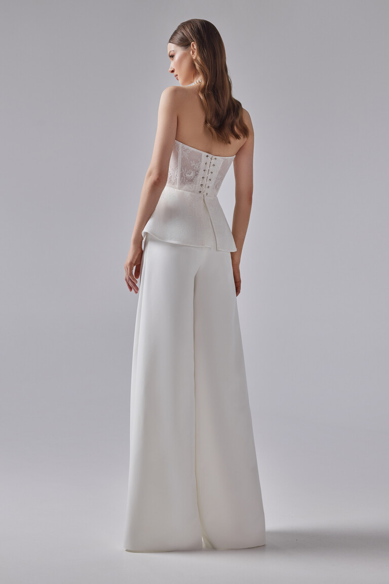 Back view of Riki bridal pantsuit highlighting the classic lace-up corset closure open back and elegant peplum hem