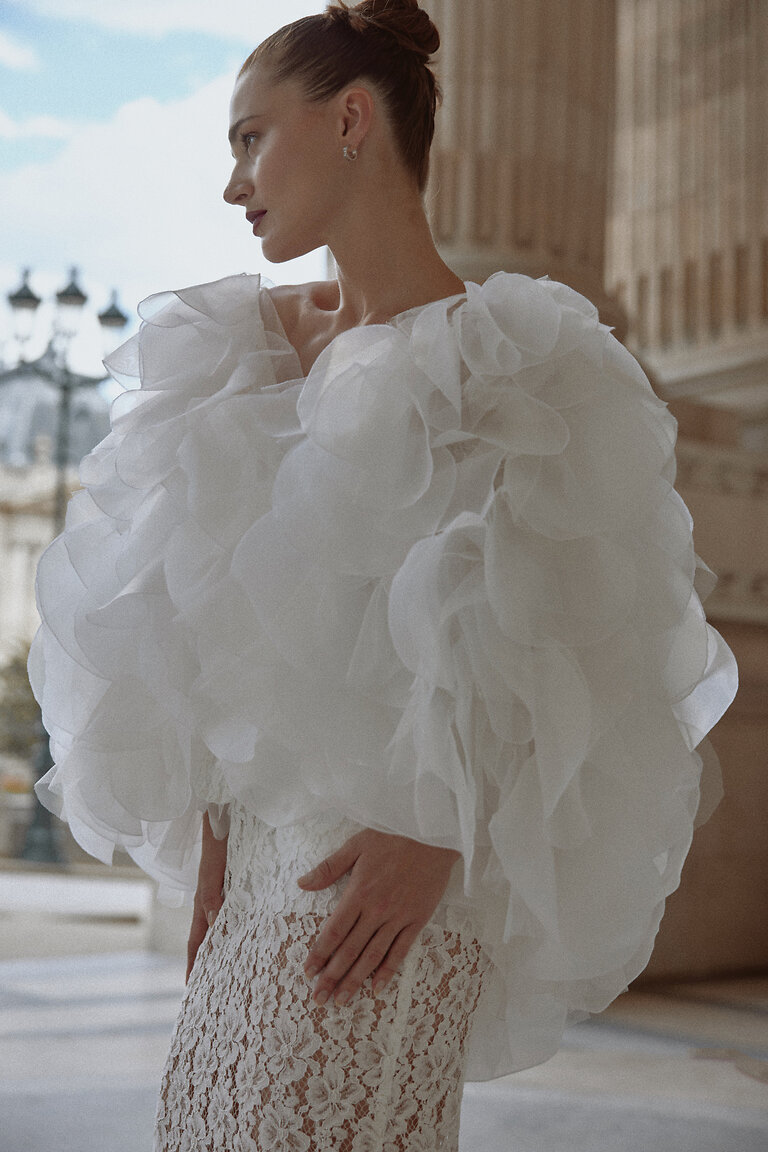 Glamorous Ruffled Bridal Cover Up Medea romantic bridal shoulder cape made of sheer off-white organza, showing the glamorous ruffled volume and texture.