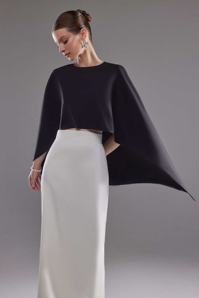 Elegant Cape Ell Black Formal Cover Up Front View Unona Cape Ell front view. Black stretch crepe evening cape with high neckline draped elegantly over a white skirt.