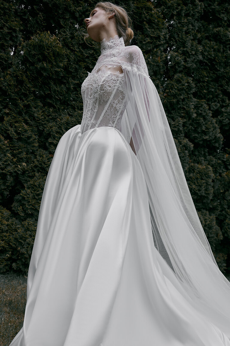 Elegant Tulle Bridal Cape Side View Side view of the romantic Evelyn tulle bridal cape with lace high neck cascading over a wedding dress.