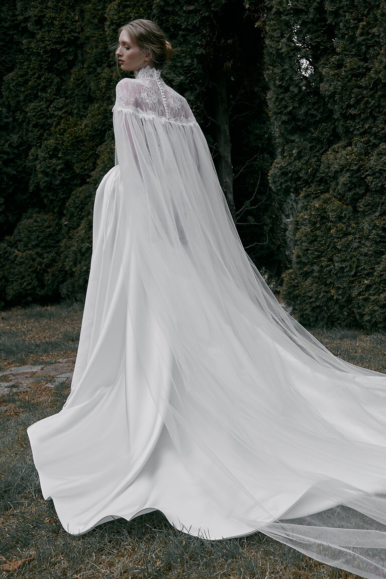 Evelyn Off-White Tulle Wedding Cape Back View Back view of off-white Evelyn bridal cape in tulle with lace details and button closure over a wedding dress.