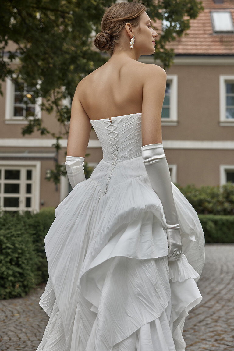 Nerina Corset Back Wedding Dress Details Back view of Unona Nerina off-white bridal gown featuring a vintage-inspired corset lace-up back and tiered skirt.