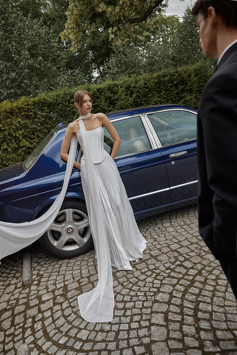 Romantic Ellora A-Line Wedding Dress Ellora off-white romantic A-line wedding dress with sweetheart neckline and pleated skirt near a car.